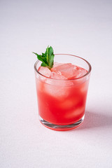 Fresh cold watermelon juice with ice cubes and green mint leaf in glass drink on white background, copy space, angle view
