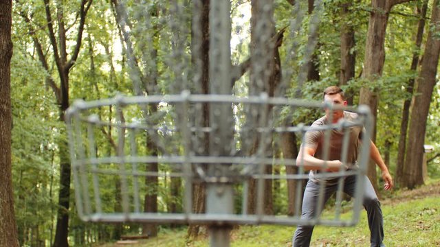 Man plays disc golf, makes putt, slow motion, focus on man