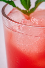 Fresh cold watermelon juice with ice cubes and green mint leaf in glass drink on white background, macro, selective focus