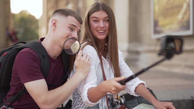 Couple of friends taking selfie with selfie stick while playing with a magnifying lens