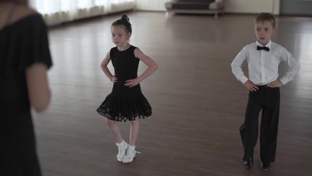 Handheld shot of a beautiful young dance teacher teaching a cute boy and a girl children how to dance in a dance class