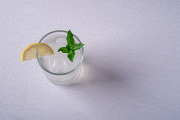 Fresh cold clear water drink in glass with ice cubes, lemon slice and mint leaf, on white gray background