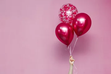 Poster stylish birthday party or holidays with balloons. three pink  balloons on pink background with copy space for text. Hand  holding three bright colorful balloons indoor. background for greeting card © mihail_pustovit