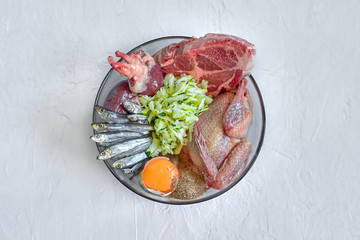 Different natural raw dog food BARF diet in bowl on white background Meat fish eggs vegetables bones organic food supplement