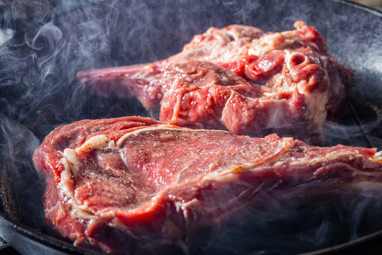 Smoke and steam rise from a beaf steak on grill pan.