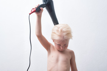 Serious blond boy with wet hair is blow dry. White background