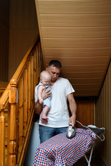 Father with a small baby in her arms ironed linen. Doing housework