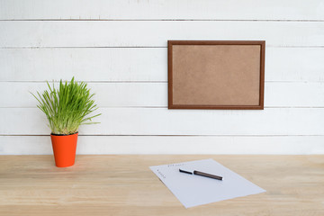 Empty frame on white wall. Sheet of paper and a pen, green houseplant on the table. Working space at home