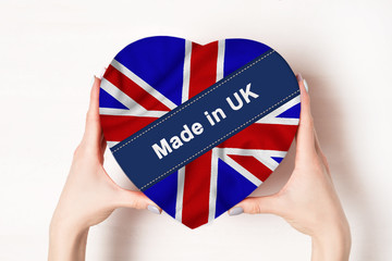 Inscription Made in UK, the flag of UK. Female hands holding a heart shaped box. White background. Place for text