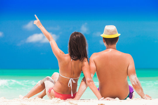Back view of a man and woman couple sitting on caribbean white sand beach