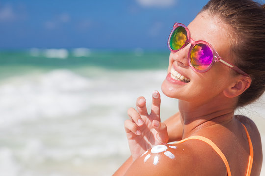 Close up of young woman in sunglasses putting sun cream on shoulder
