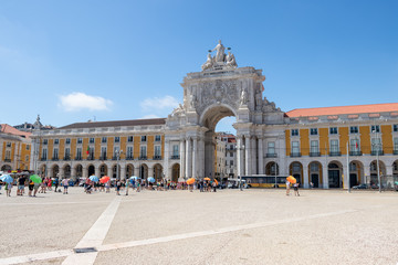 Fototapeta na wymiar Commerce Square (Praça do Comércio in Portuguese) in Lisbon, Portugal with anonymous tourists and tour operators with colored umbrellas. People's faces intentionally blurred