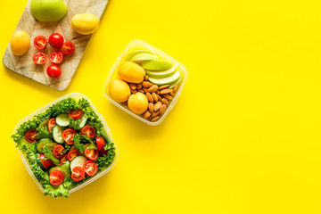 food container with salad and nuts, fruit on yellow background top view mockup