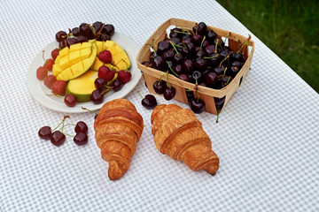 Fruit salad with fresh sweet cherry, mango and croissants on the table  white background. Flat lay, concept composition brackfast