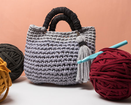 Bolso gris y negro hecho a mano con trapillo junto a bolas de tela de trapillo de colores