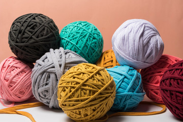 Bolas de trapillo de colores azules, amarillo beige y cafés sobre un fondo color  coral por...