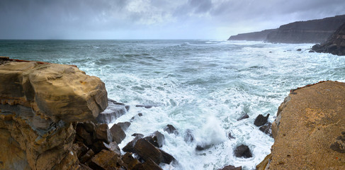 A huge ocean waves breaking on the coastal cliffs in at the cloudy stormy day. Breathtaking romantic panoramic seascape of ocean coastline. Peniche, Portugal.