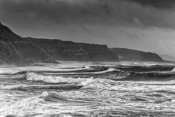 A huge ocean waves breaking on the coastal cliffs in at the cloudy stormy day. Breathtaking romantic seascape of ocean coastline. Bw photo.