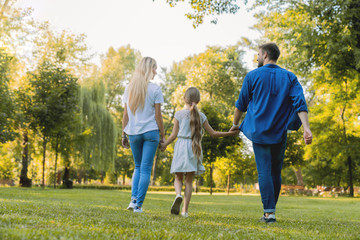 Fototapeta premium Rear view of parents and cute daughter having fun and walking at city park