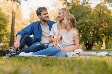 Fototapeta premium Beautiful happy family enjoying moment while sitting on blanket in park