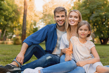 Fototapeta premium Beautiful happy family enjoying moment while sitting on blanket in park and looking at camera
