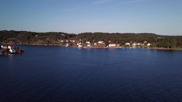 Aerial, drone shot, over the sea, towards buildings, in Ronnes town, near Grimstad city, on a sunny day, in Aust Agder, Norway