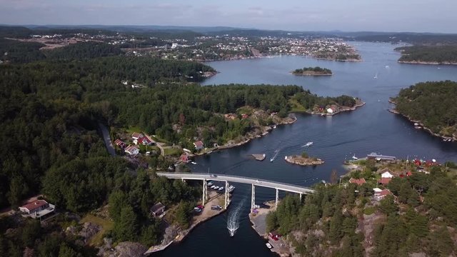 Aerial, tilt up, drone shot of the Blindleia inland waterway, strait, overlooking the bridge to Justoya, boats, the Skaueroya and Lillesand city, on a sunny day, in Aust Agder, Norway
