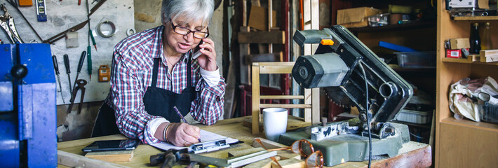 Fototapeta na wymiar Senior female carpenter talking on the phone in her workshop