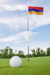 Obraz premium Armenia flag on golf course putting green with a ball near the hole