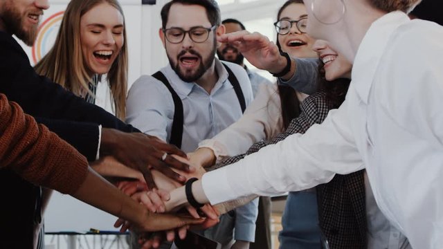 Close-up young male boss joining hands with multiethnic team celebrating success at modern office slow motion RED EPIC.
