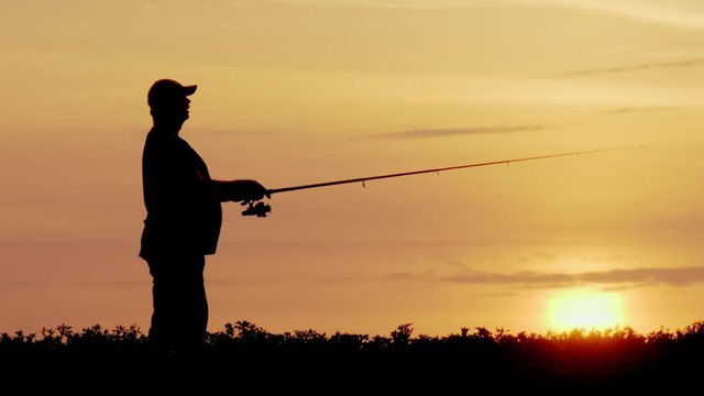 Silhouette of fisherman fishing at sunset with spinning rod. Fishman throws fishing tackle.
