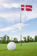 Obraz premium Denmark flag on golf course putting green with a ball near the hole