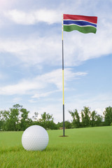 Obraz premium Gambia flag on golf course putting green with a ball near the hole
