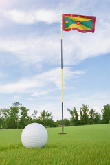 Obraz premium Grenada flag on golf course putting green with a ball near the hole