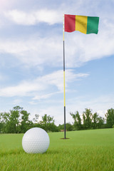 Obraz premium Guinea flag on golf course putting green with a ball near the hole