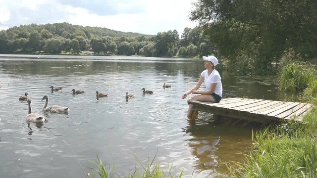 A young woman feeding on a lake swans and ducks Bird feeding in summer day