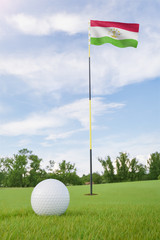 Obraz premium Tajikistan flag on golf course putting green with a ball near the hole