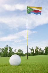 Obraz premium The Comoros flag on golf course putting green with a ball near the hole