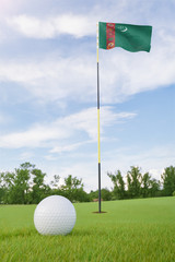 Obraz premium Turkmenistan flag on golf course putting green with a ball near the hole