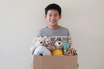 Mixed Asian young volunteer preteen teenage boy holding a box full of used toys, cloths, books and...
