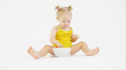 Funny baby girl eats her meal with a spoon