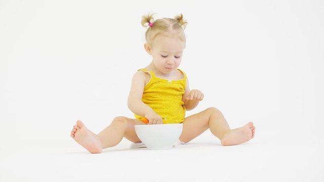 Funny baby girl eats her meal with a spoon