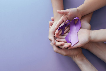 Adult and child hands holding purple ribbons  on purple background, Alzheimer's disease, Pancreatic...