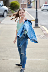 Stunning young female model walks on street in green blouse and blue jeans