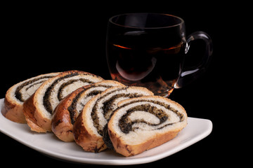 Poppy seed roll and tea in a glass mug. Isolated on black background