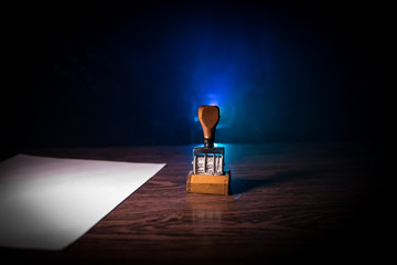 Close up view of rubber date stamper on wooden table with dark toned foggy background.