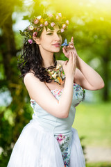 Portrait Smiling Sensual Brunette Female in White Dress Outdoors. Posing with Flowery Chaplet and Butterfly Against Sunlight.