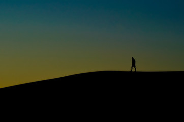 Silhouettes of man walking through dunes