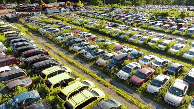 Rising aerial above hundreds of abandoned, crashed vehicles in junkyard awaiting recycling