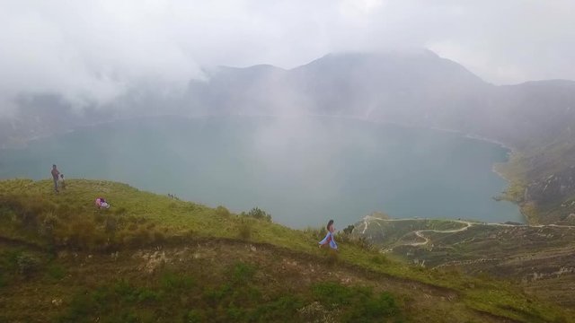 A beautiful woman runs along the rim of a volcano and cone at Quilotoa, Ecuador.